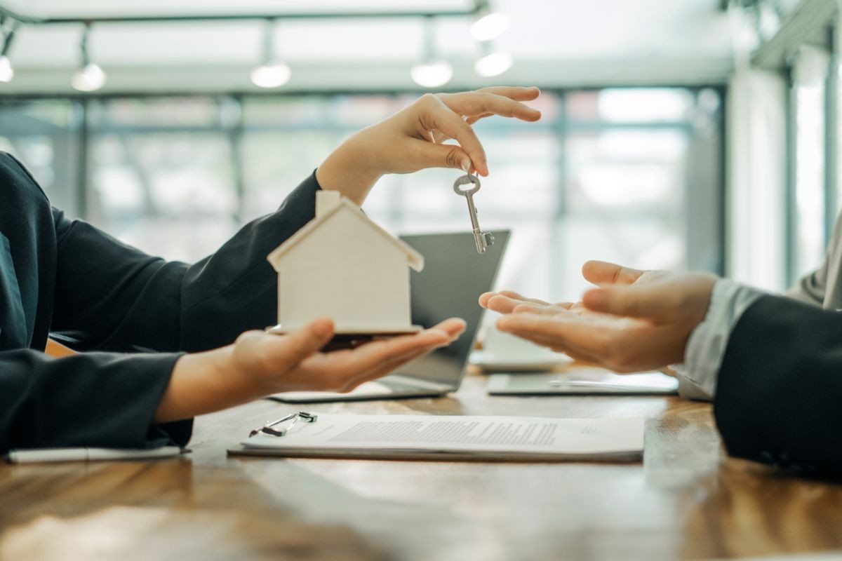 Real estate agents holding model house and keys for submit documents for customers to sign for a sale contract,real estate concept.